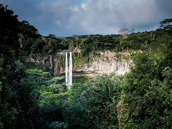 A distant view of a waterfall with a jungle surrounding it.