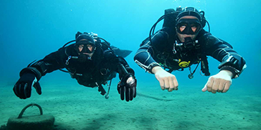 Two divers approach the camera in clear waters.