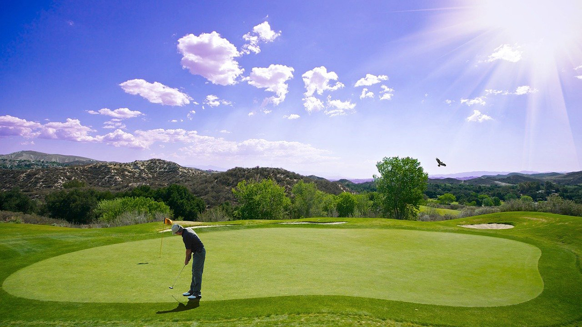 A Pristene view of a golf course with a sky-high sun looking down on a golfer.