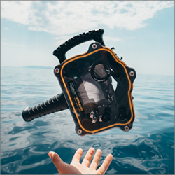 a hand holding a diving camera in front of an ocean