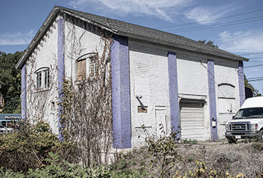 A White building with periwinkle supports with a truck parked outside of it.